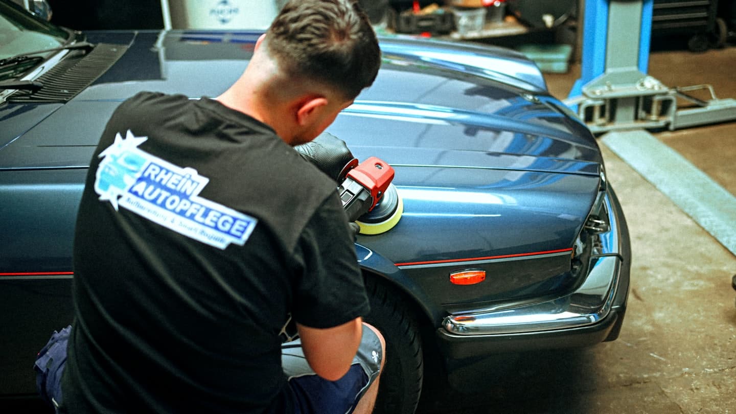 Profesionální detailista leští tmavě modrý klasický vůz v garáži.