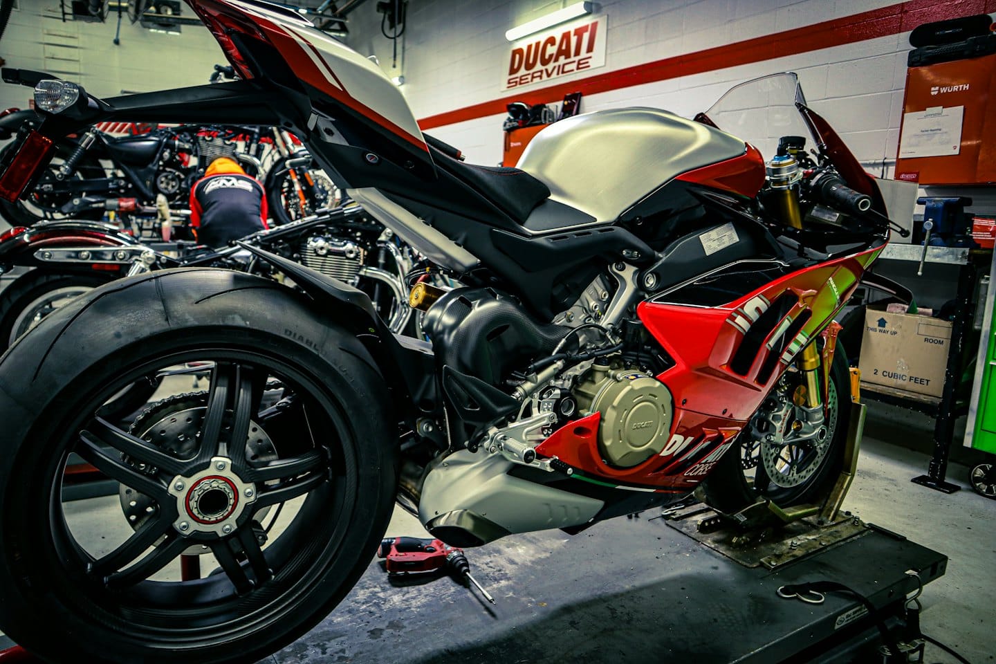 Červený, bílý a stříbrný sportovní motocykl na servisním stojanu v garáži.